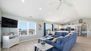 A modern living room with a sectional sofa, a flat-screen TV, and a dining area with a kitchen in the background.