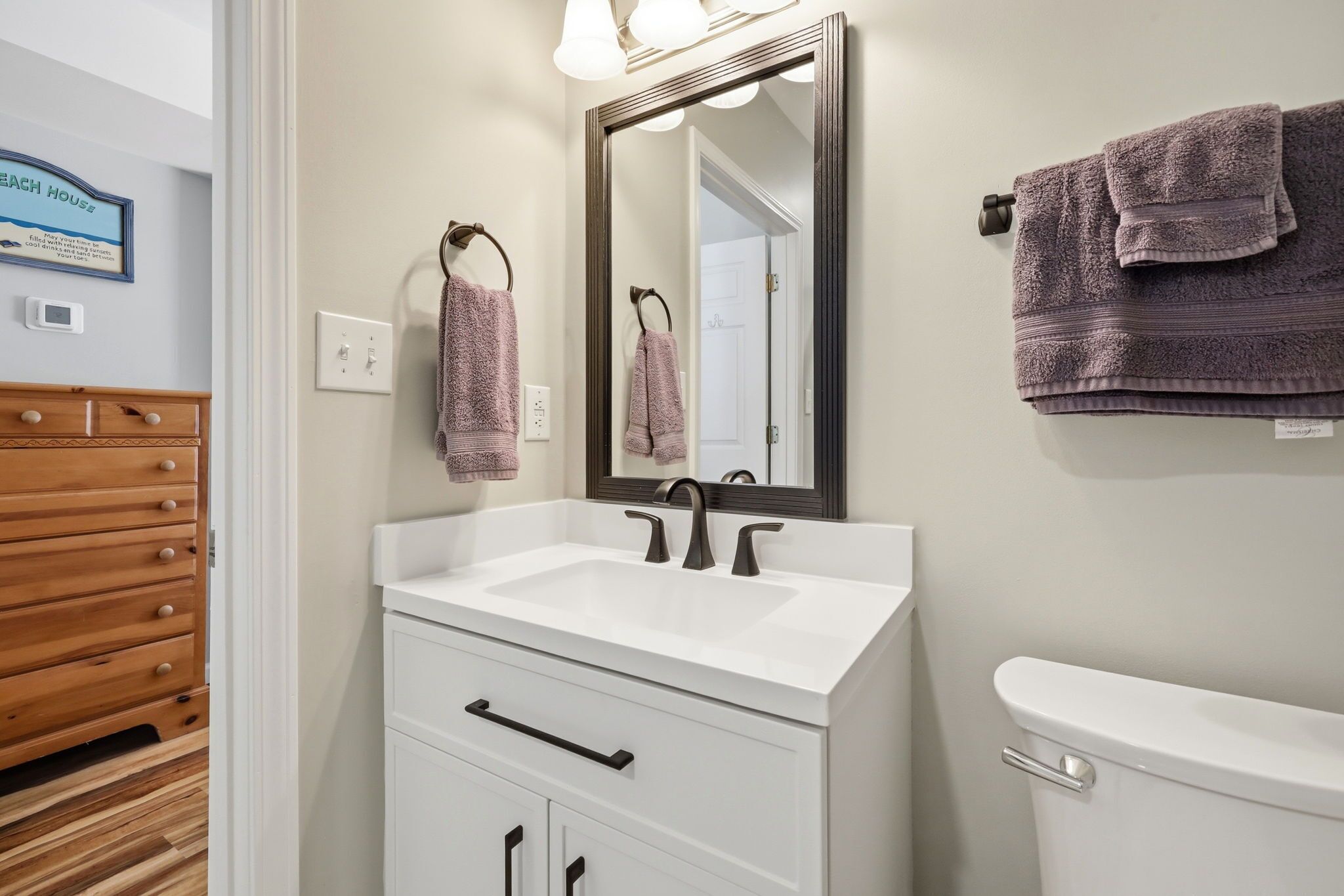 Une salle de bain avec un lavabo blanc, un miroir, des toilettes et un meuble en bois doté de tiroirs.