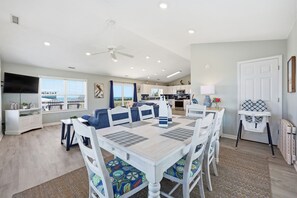 A modern kitchen with white cabinets, a microwave, and a dining area with a white table and blue chairs. - Barefoot Pelican| Pool, Bikes & Game Room (Emerald Isle)