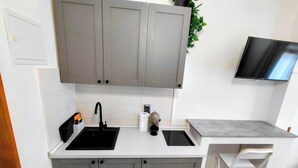 A compact kitchen with grey cabinets, a black sink, a small countertop, and a white chair. - Adorable studio apartment with AC in charming Grebaštica perfect for getaway (Grebaštica)