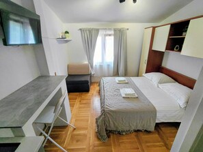 A compact hotel room with a bed, a desk, a television, and a window with curtains. - Adorable studio apartment with AC in charming Grebaštica perfect for getaway (Grebaštica)