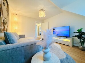 A modern living room with a grey sofa, a round coffee table, a TV on a stand, and a large painting on the wall.