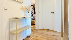 Ein Flur mit Holzboden, einem weißen Konsolentisch mit Dekoration und einem gerahmten Kunstwerk an der Wand.