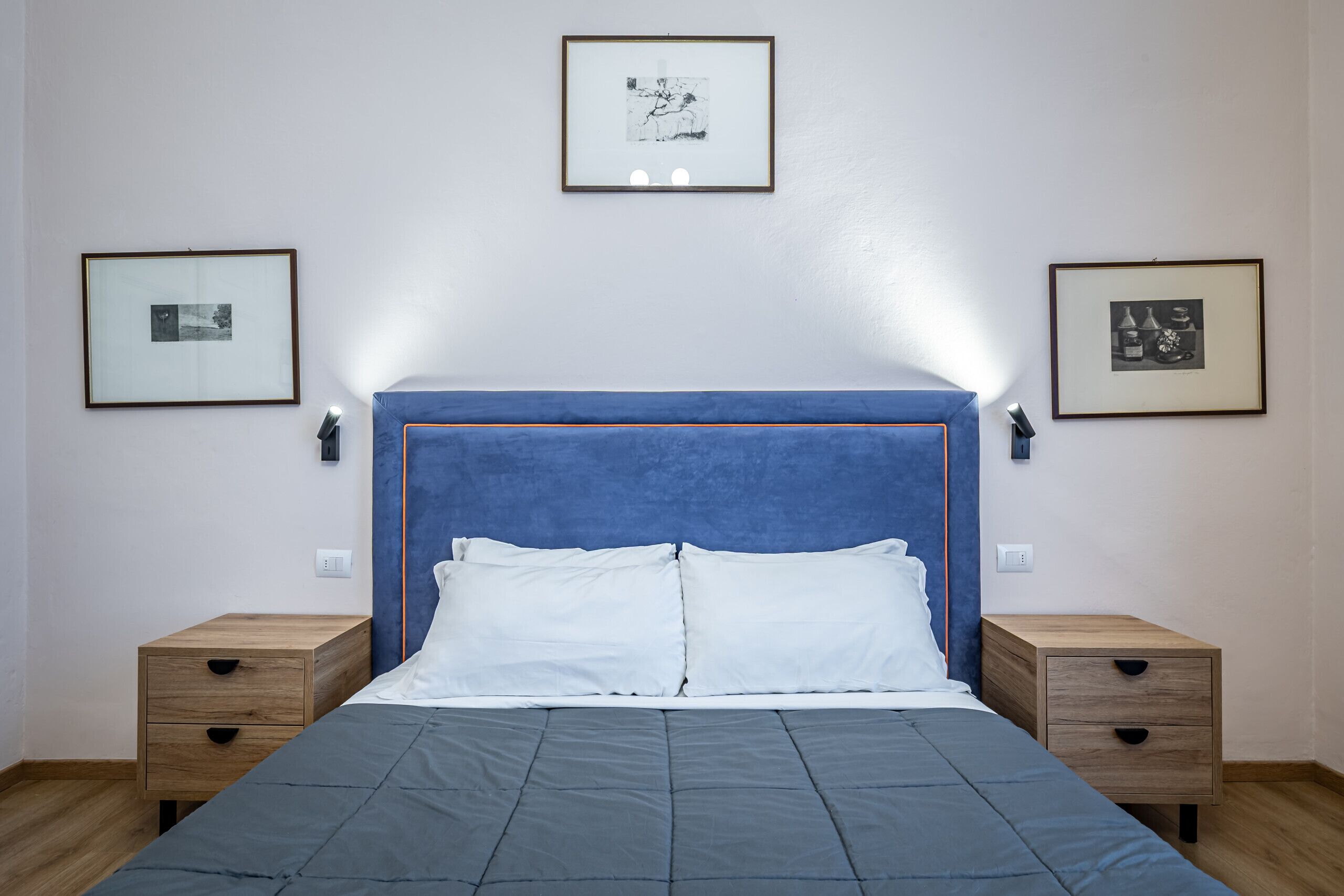 Een slaapkamer met een bed, twee nachtkastjes en drie ingekaderde foto’s aan de muur.