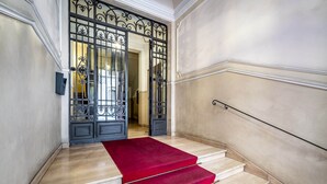 A grand staircase with a red carpet leading to a large ornate door. - Five Suites Mantellate (Florence)