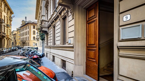 A street view with parked cars and a building with a wooden door and a number '9' sign. - Five Suites Mantellate (Florence)