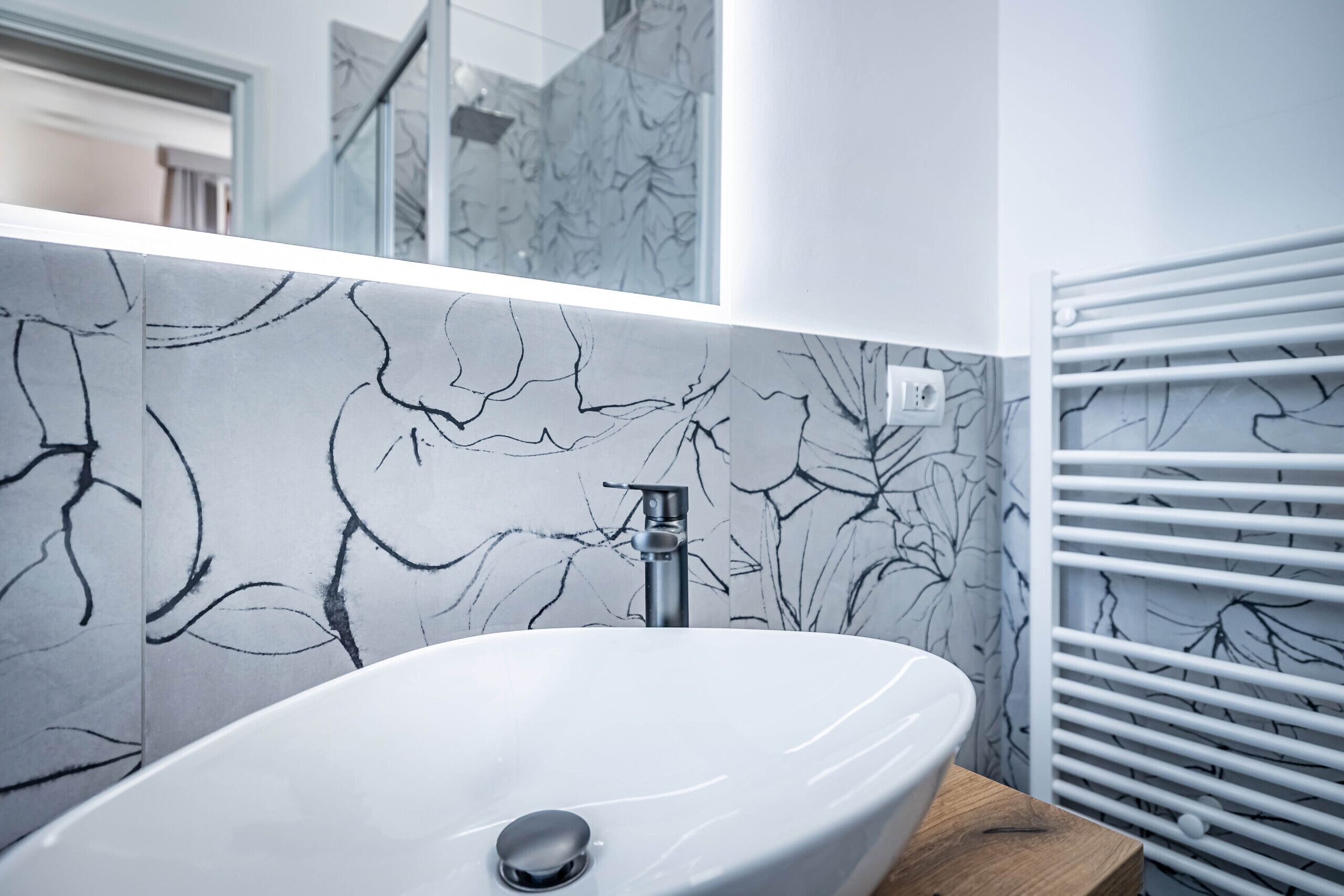 A modern bathroom with a white sink, marble-patterned walls, and a wooden countertop.