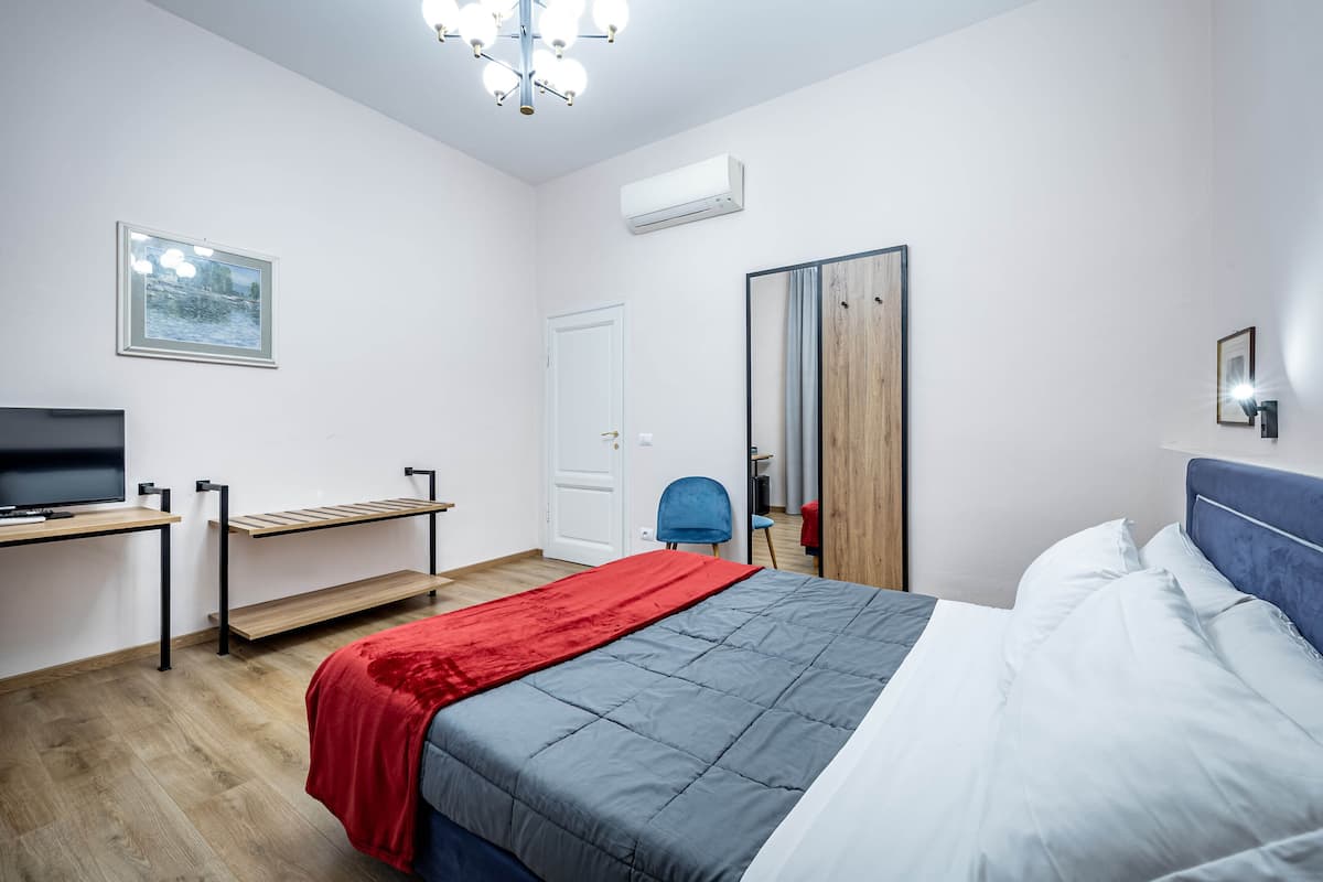 A modern bedroom with a bed, a desk, a chair, and a TV.