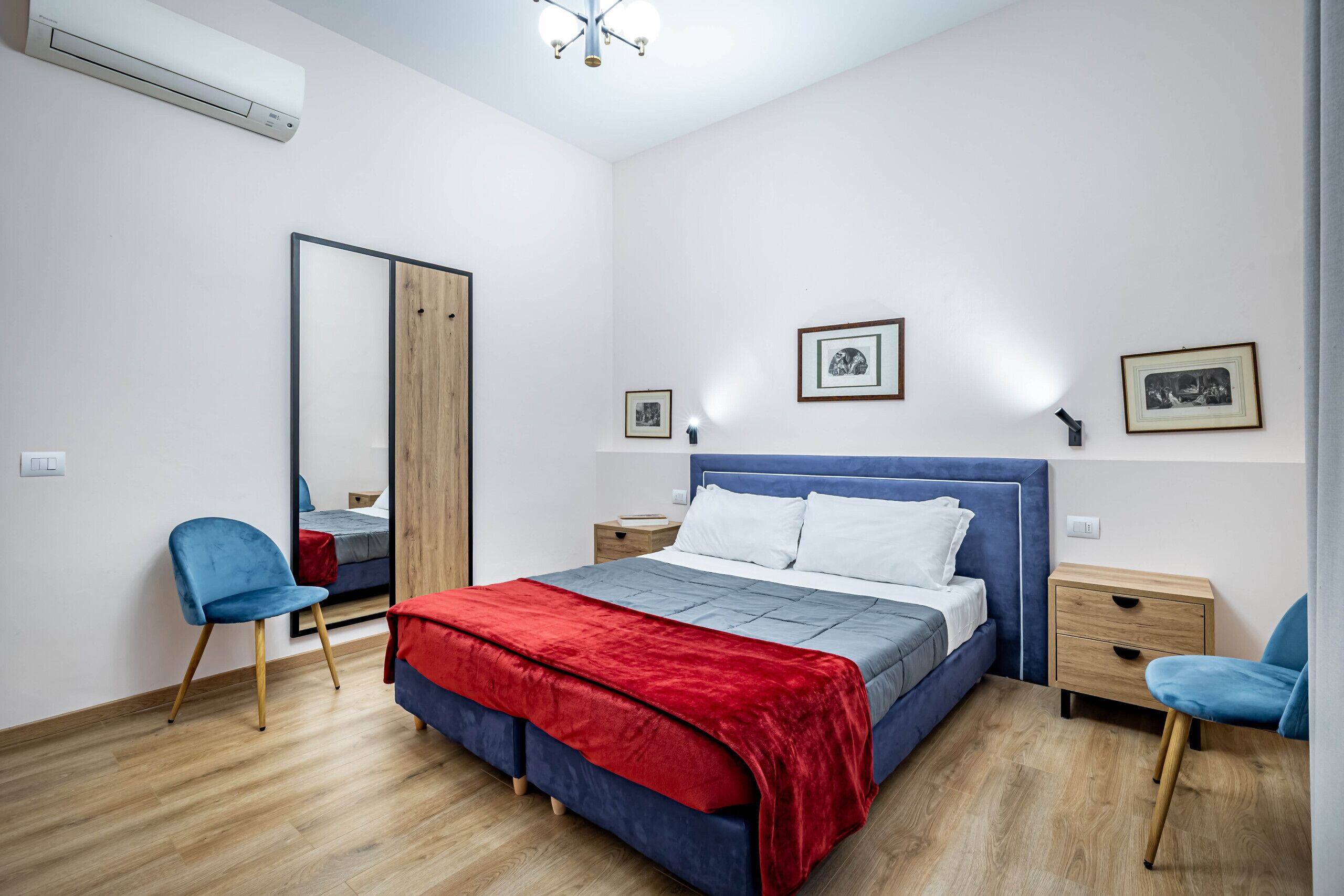 Une chambre à coucher comprenant un lit, deux chaises, une table de chevet, un miroir et deux tableaux encadrés accrochés au mur.