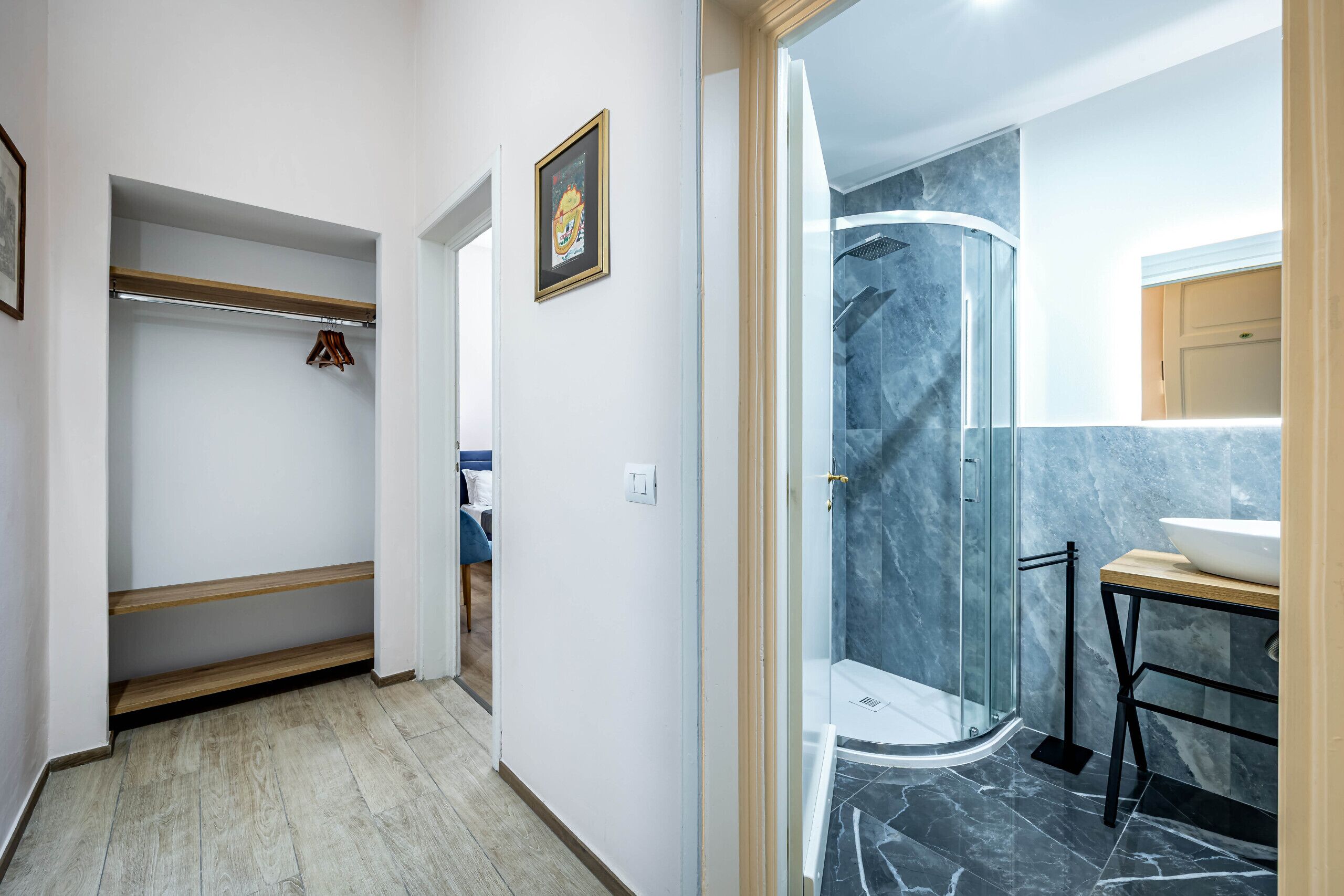 A hallway with a closet, a framed picture, and a bathroom with a shower and sink.