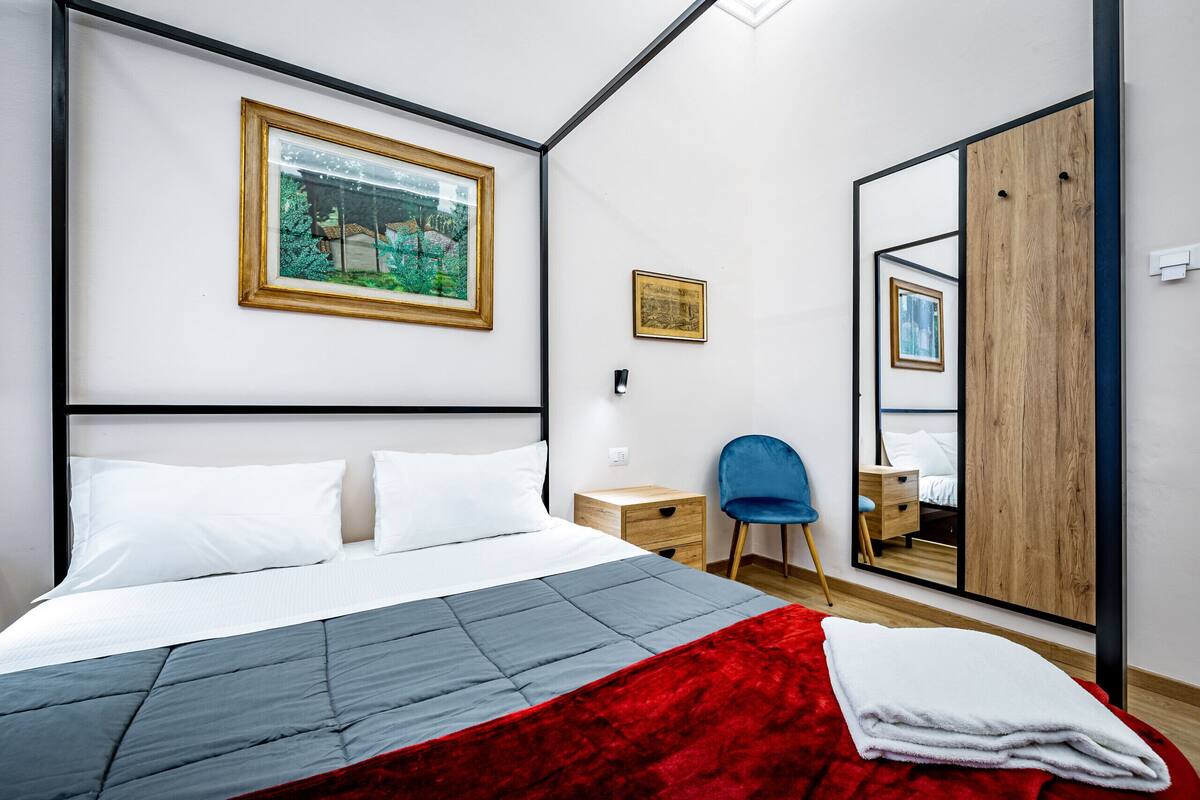 A bedroom with a bed, a chair, a wardrobe, and a mirror.