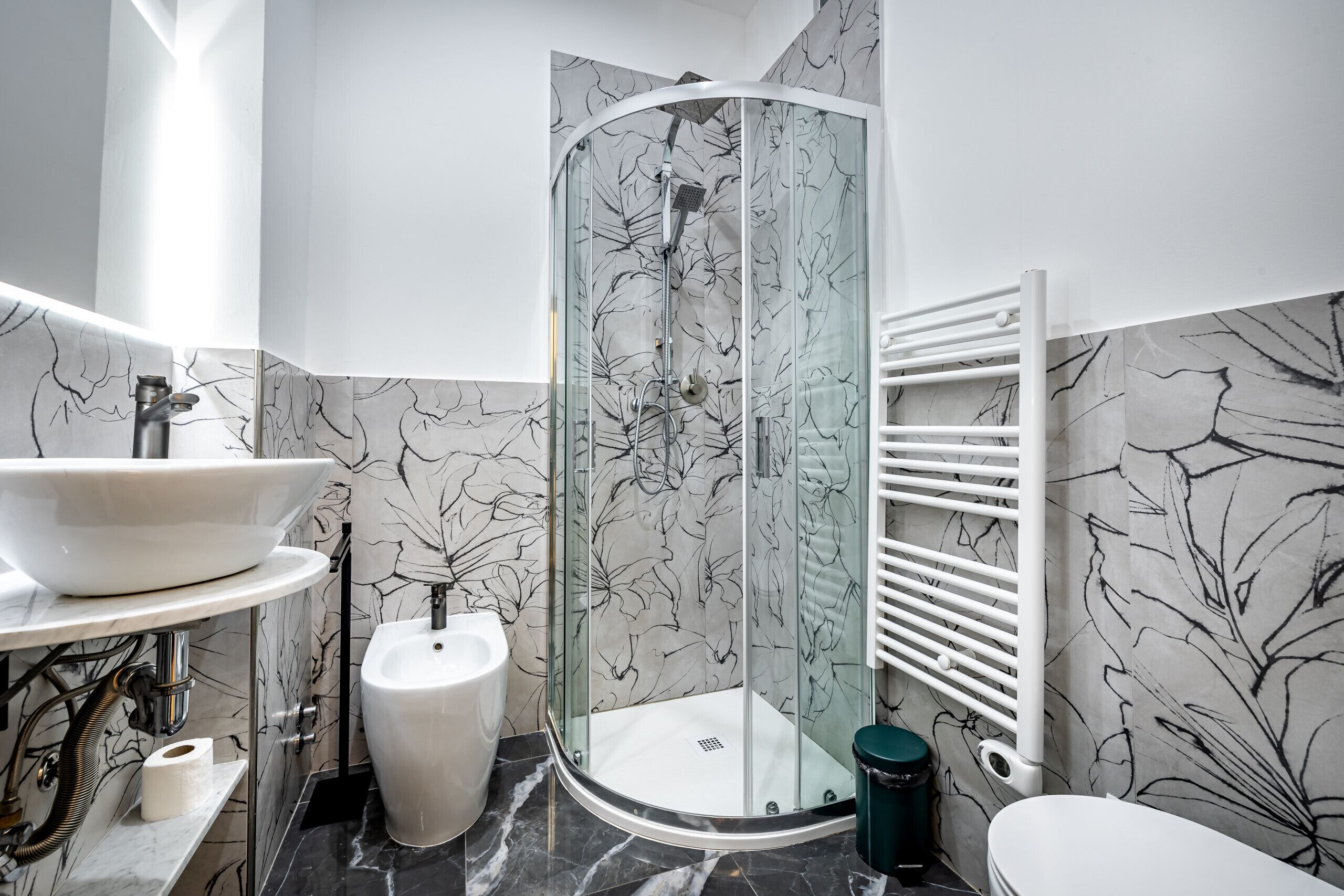 Un bany modern amb un espai de dutxa de vidre, un lavabo blanc, un vàter i un sòl de rajola de marbre.