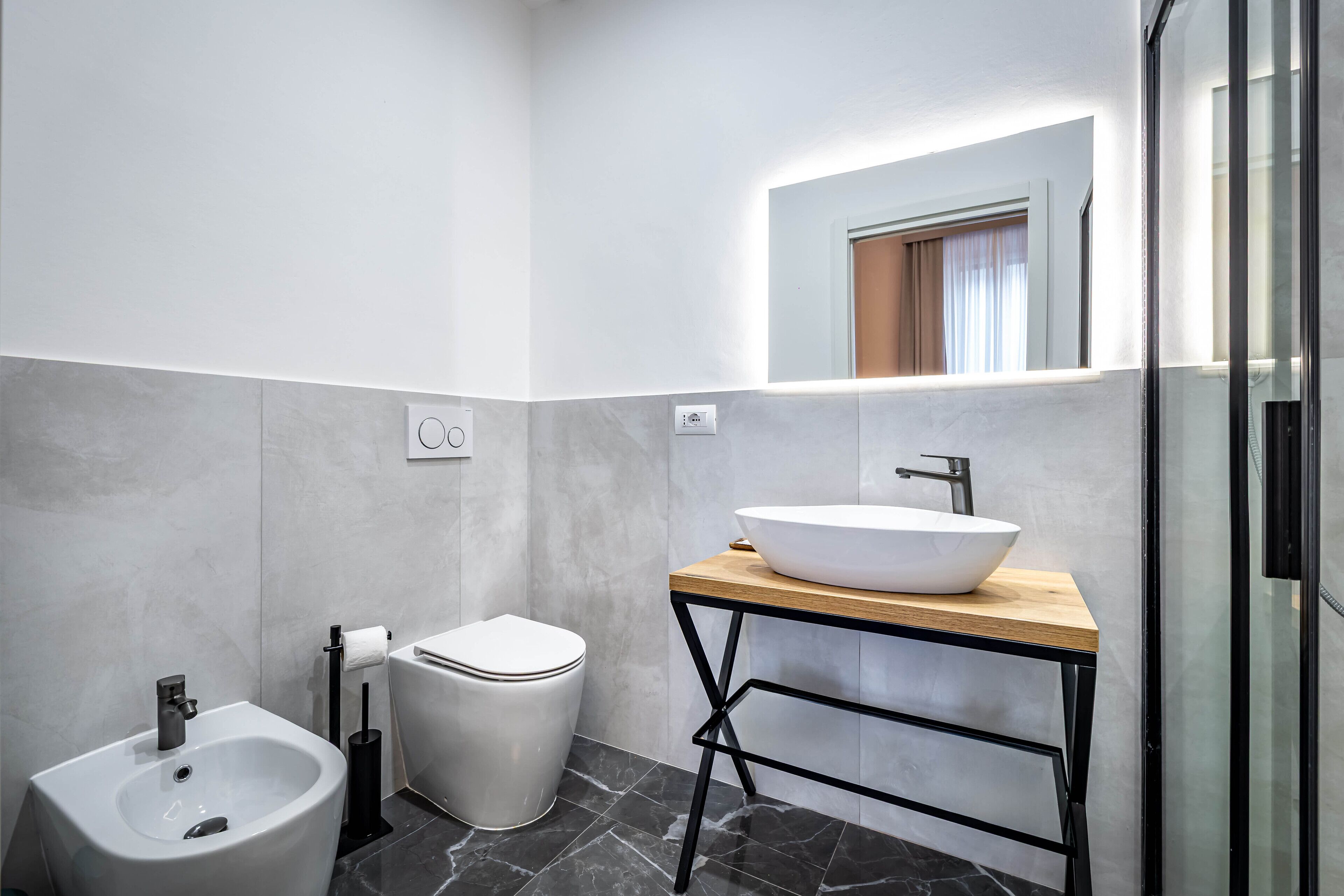 A modern bathroom with a bidet, toilet, and a large mirror above a wooden vanity with a white sink.
