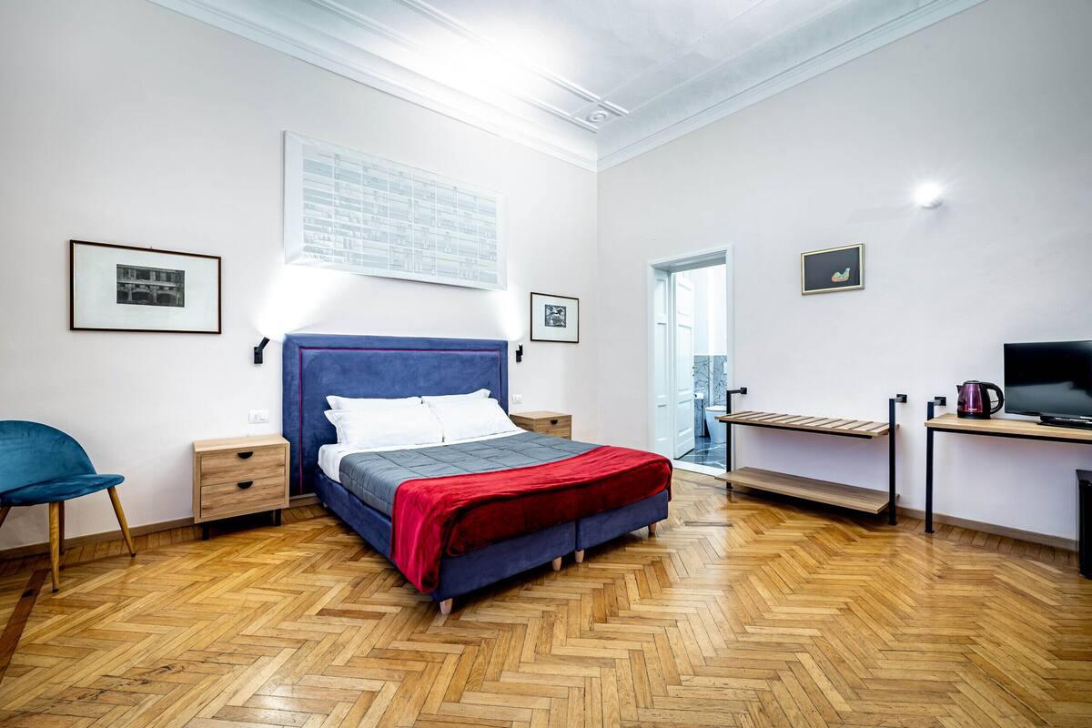 A bedroom with a bed, a chair, a desk, and a television.