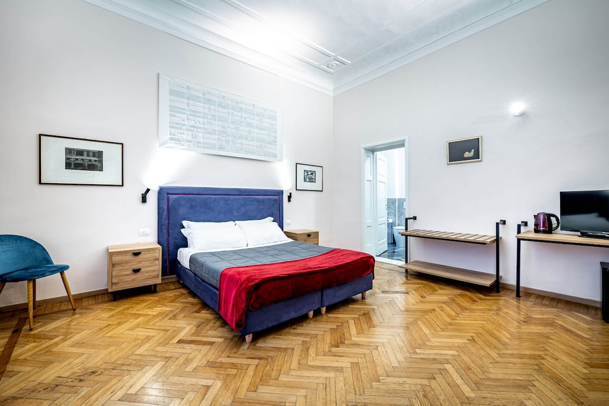Ein Schlafzimmer mit einem Bett, einem Sessel, einem Schreibtisch und einem Fernseher.