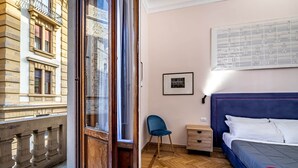 A room with a bed, a chair, a nightstand, a window, and a view of a building. - Five Suites Mantellate (Florence)