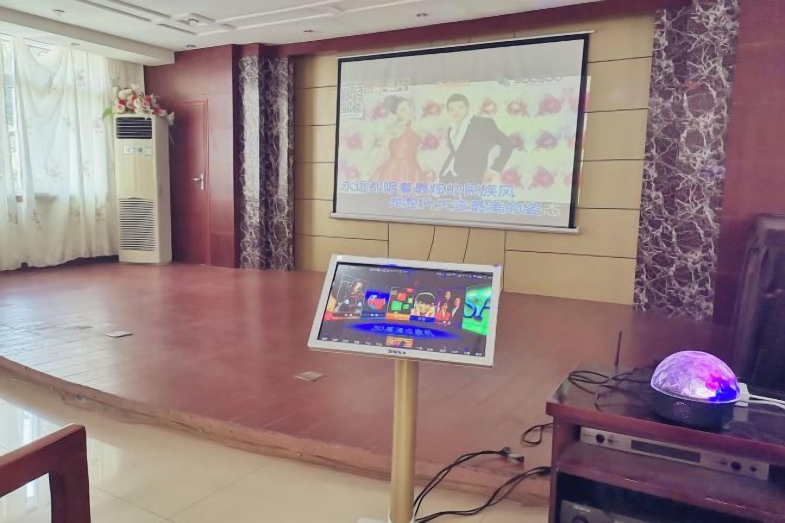 Un salón de conferencias con un escenario, una pantalla de proyección y una pantalla digital.