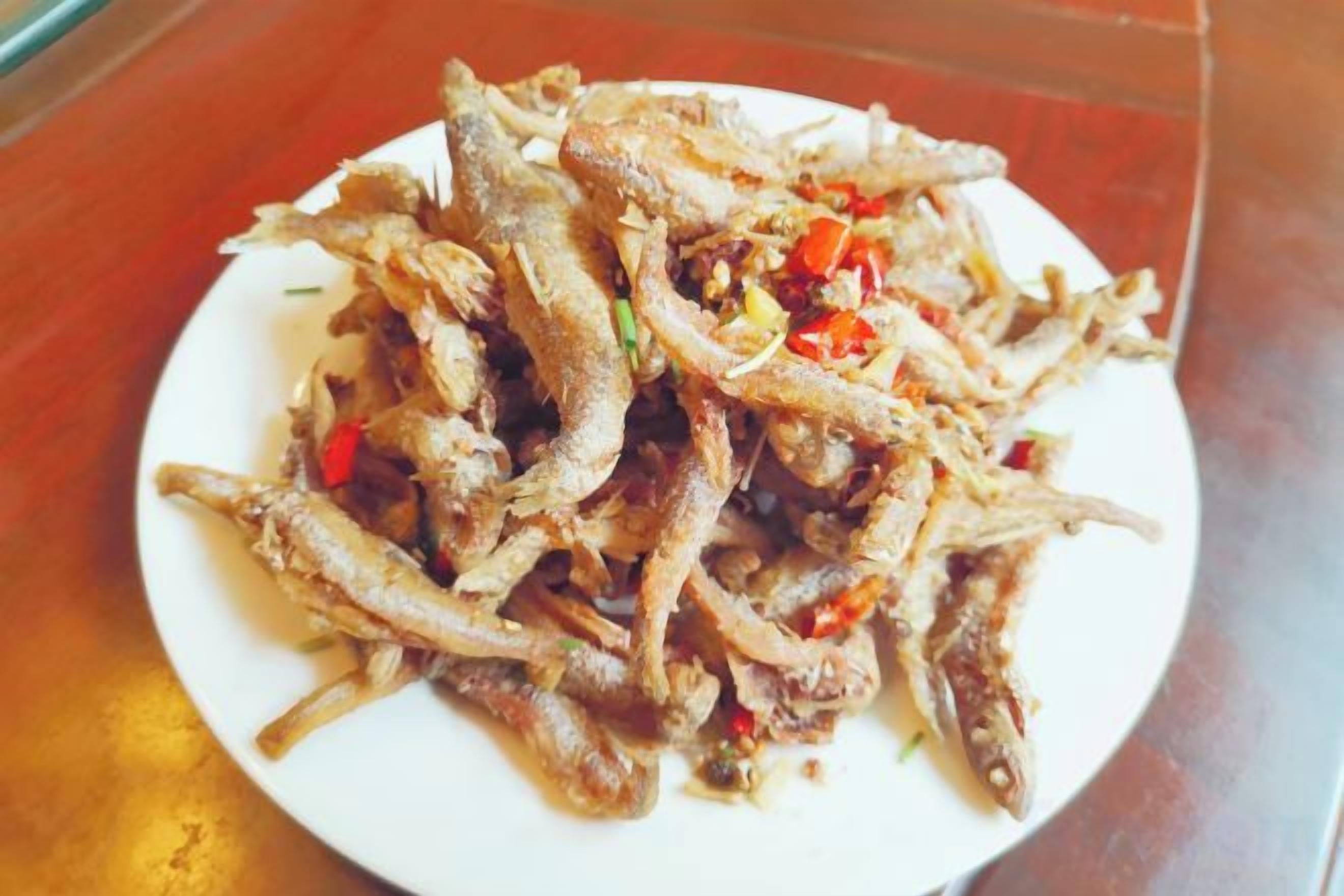 A plate of fried fish with red chili flakes.