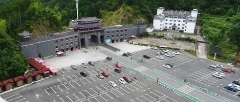 A large parking lot with multiple rows of parking spaces, a building with a traditional architectural style, and a mountainous backdrop.