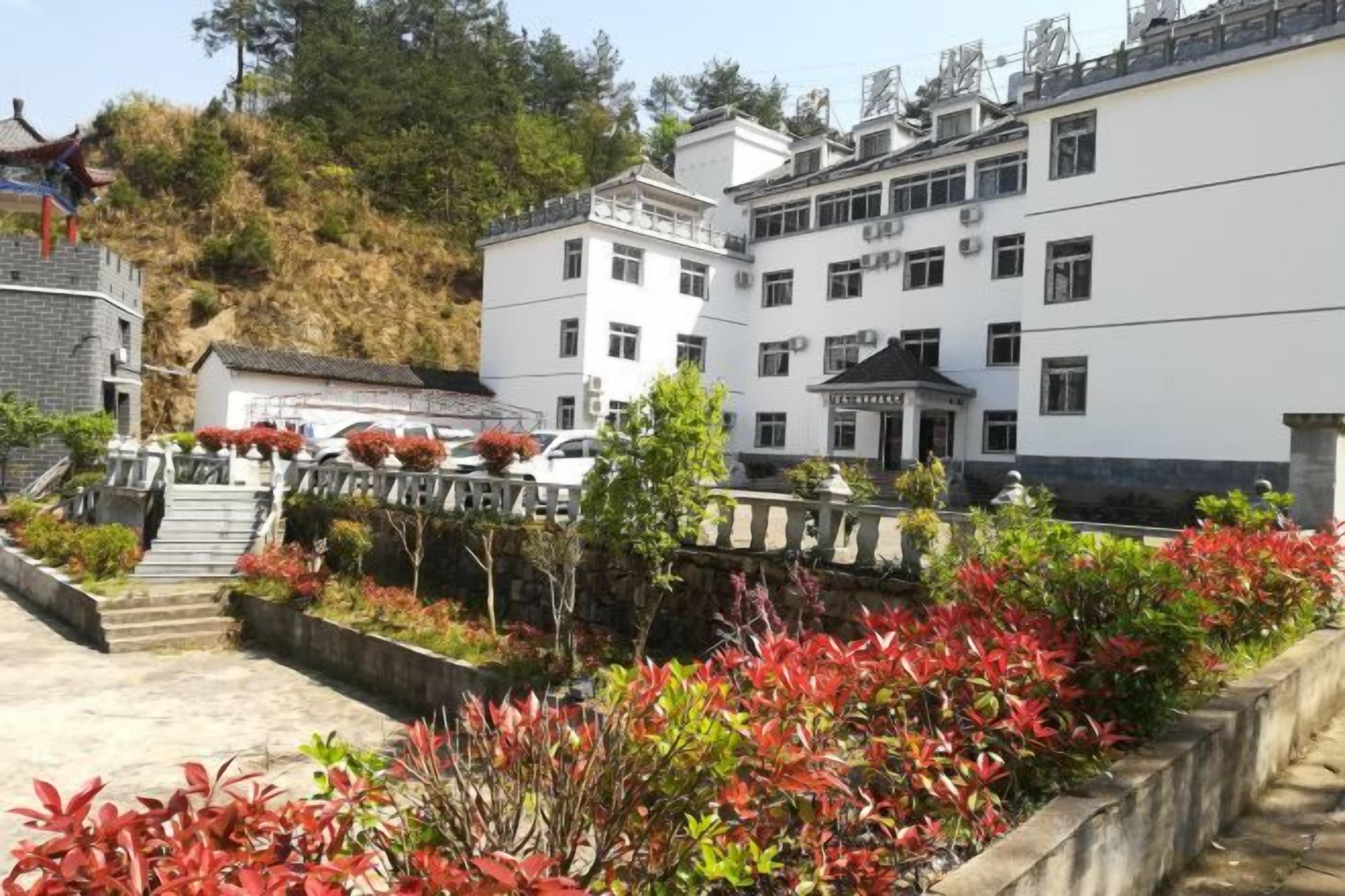 Un edificio tradicional de varios pisos, una escalera que conduce a la entrada y un jardín bien cuidado con follaje rojo.