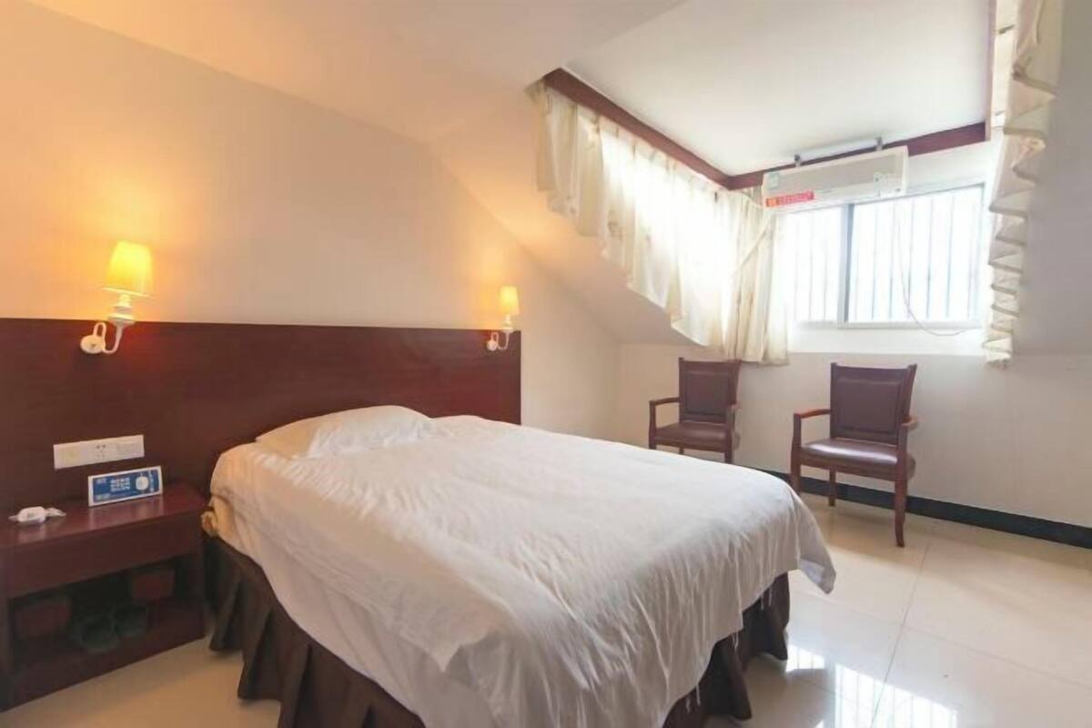 Habitación de hotel con cama, dos sillas, una mesita de noche y aire acondicionado instalado en la pared.