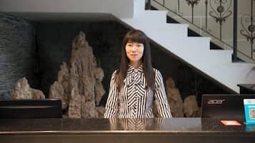 A reception desk with a laptop, a stone wall, and a staircase in the background.