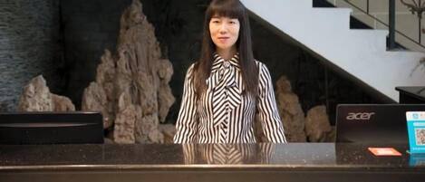A reception desk with a laptop, a stone wall, and a staircase in the background.