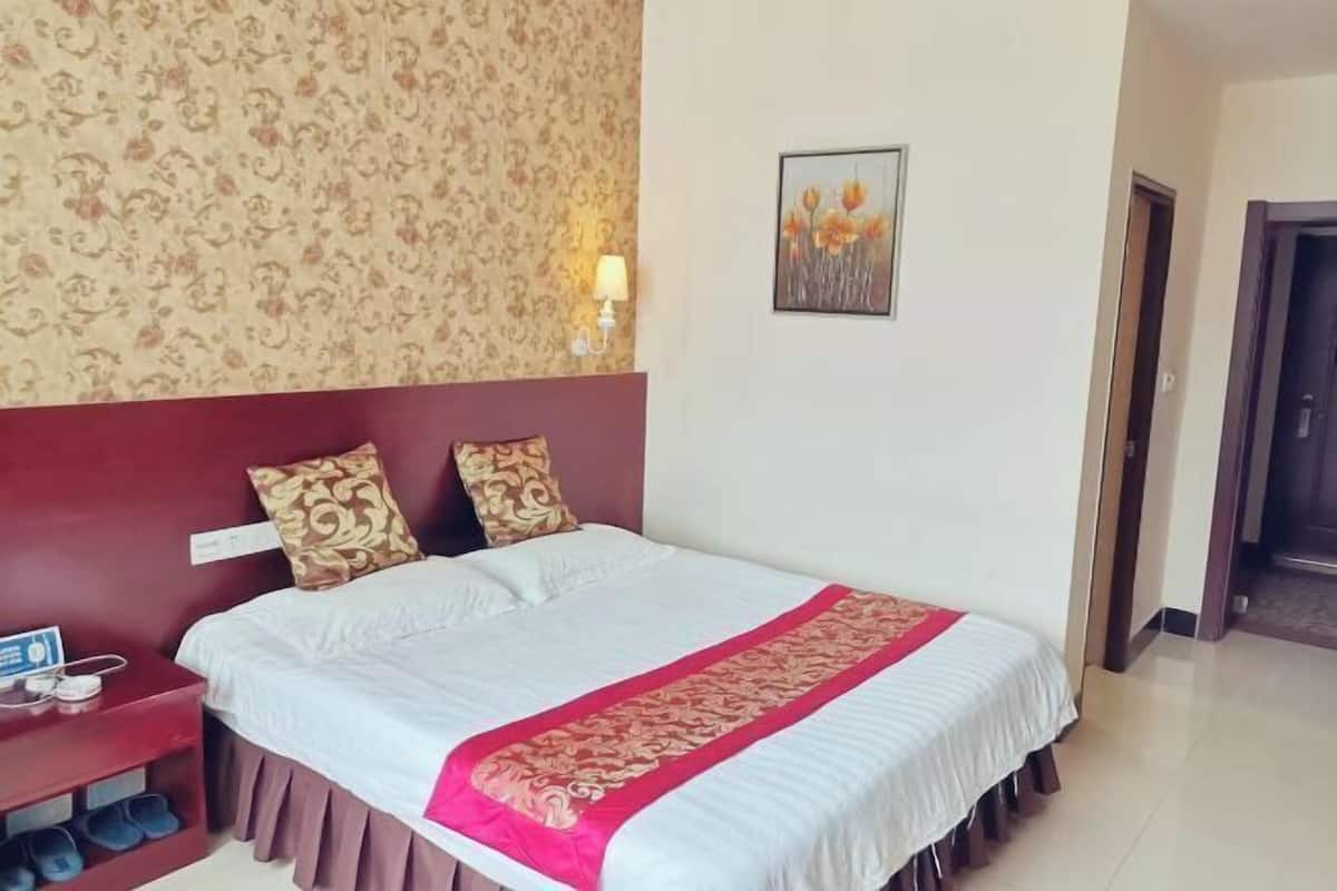 Habitación de hotel con una cama grande, una mesita de noche con lámpara y una pared con estampado floral.