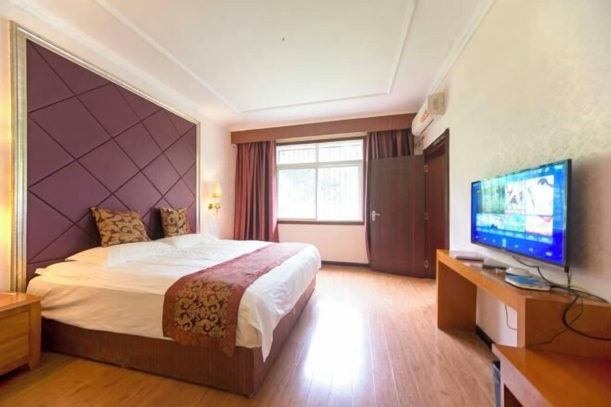 Una habitación de hotel con una cama grande, televisión y ventana con cortinas.