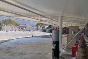 A covered parking area with a large building in the background, a green bus, and a red barrier. - Junyi Nanshan Hotel, Luotian (Luotian County)