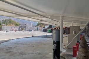 Un área de estacionamiento techada con un edificio grande al fondo, un autobús verde y una barrera roja.