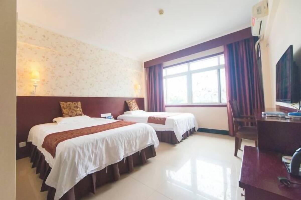 Habitación de hotel con dos camas, un escritorio, un televisor y una ventana con cortinas.