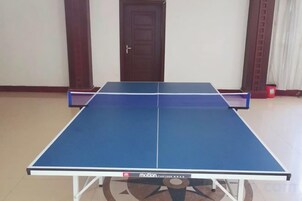 Una mesa de ping pong con superficie azul y red, ubicada en una habitación con puerta de madera y pared blanca.