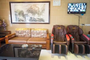 Una habitación con un sofá marrón, sillones de masaje, un televisor y una obra de arte enmarcada en la pared.