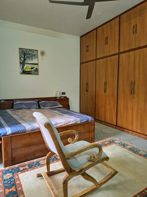 A bedroom with a wooden bed, a wooden chair, a large wardrobe, and a painting on the wall.