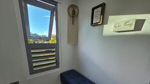 Ein Zimmer mit Fenster, einer blauen Bank, einem an der Wand befestigten Regal mit einem Schild und einem dekorativen Gegenstand.