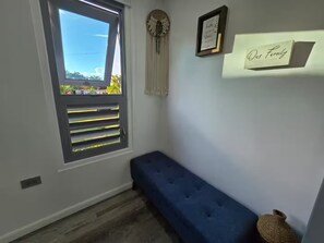 A room with a window, a blue bench, a wall-mounted shelf with a sign, and a decorative item. - The Palms Container House (San Antonio)