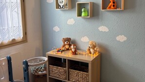 A child's playroom with a crib, a small table with toys, and wall decorations including a whale and cloud patterns.