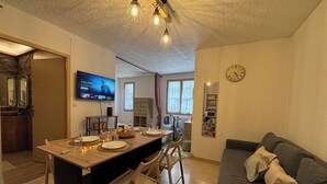 A modern kitchen with a dining area, a sofa, and a TV mounted on the wall.