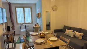 A cozy living room with a dining area, a sofa, a clock, and a window with curtains.