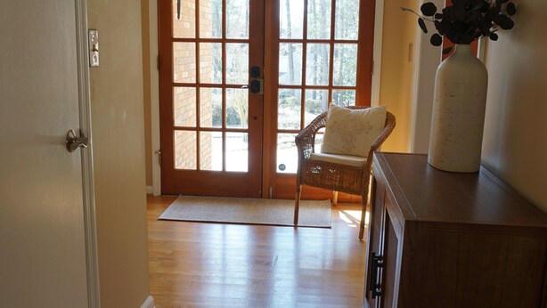 A hallway with wooden flooring, a wicker chair, a white vase, and a door leading to a bright room with a window. - Home in North Augusta (North Augusta)