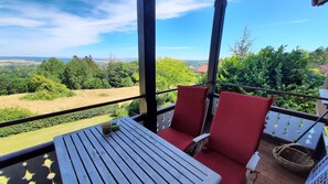 A balcony with a table and two red chairs, overlooking a scenic landscape with trees and fields. - Villa Silberborn, Apt. 9: A Dream for Two (Bad Harzburg)