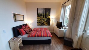 Una camera da letto con un letto, una TV, un quadro, una lampada e una finestra.