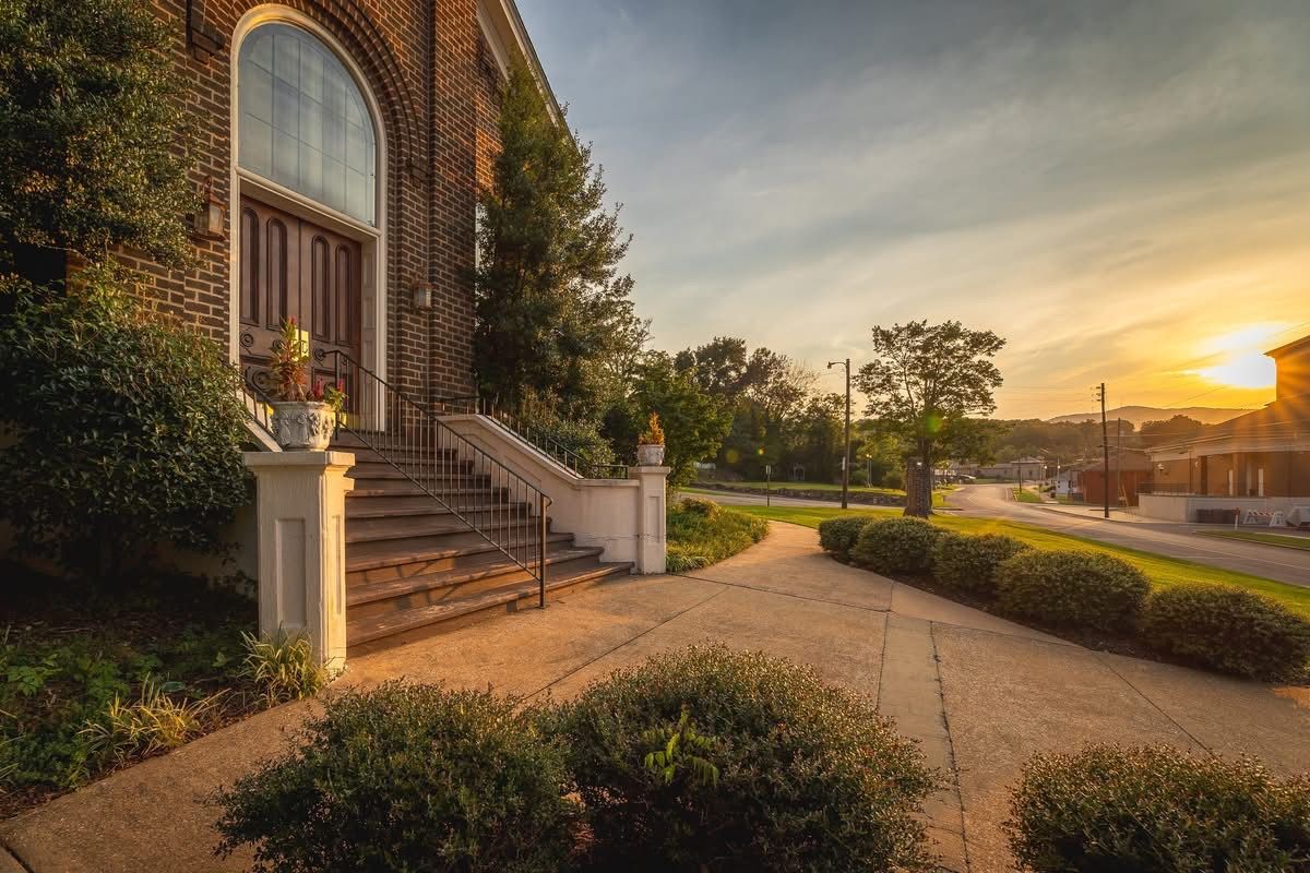 A residential house with a brick facade, a large arched window, and a front porch with steps leading to a door.