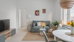 Ein modernes Wohnzimmer mit einer Couch, einem Fernseher, einer Lampe und einem Essbereich mit Tisch und Stühlen.