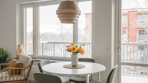 Ein runder Esstisch mit Stühlen, eine Blumenvase, eine Pendelleuchte und Blick auf einen verschneiten Balkon.
