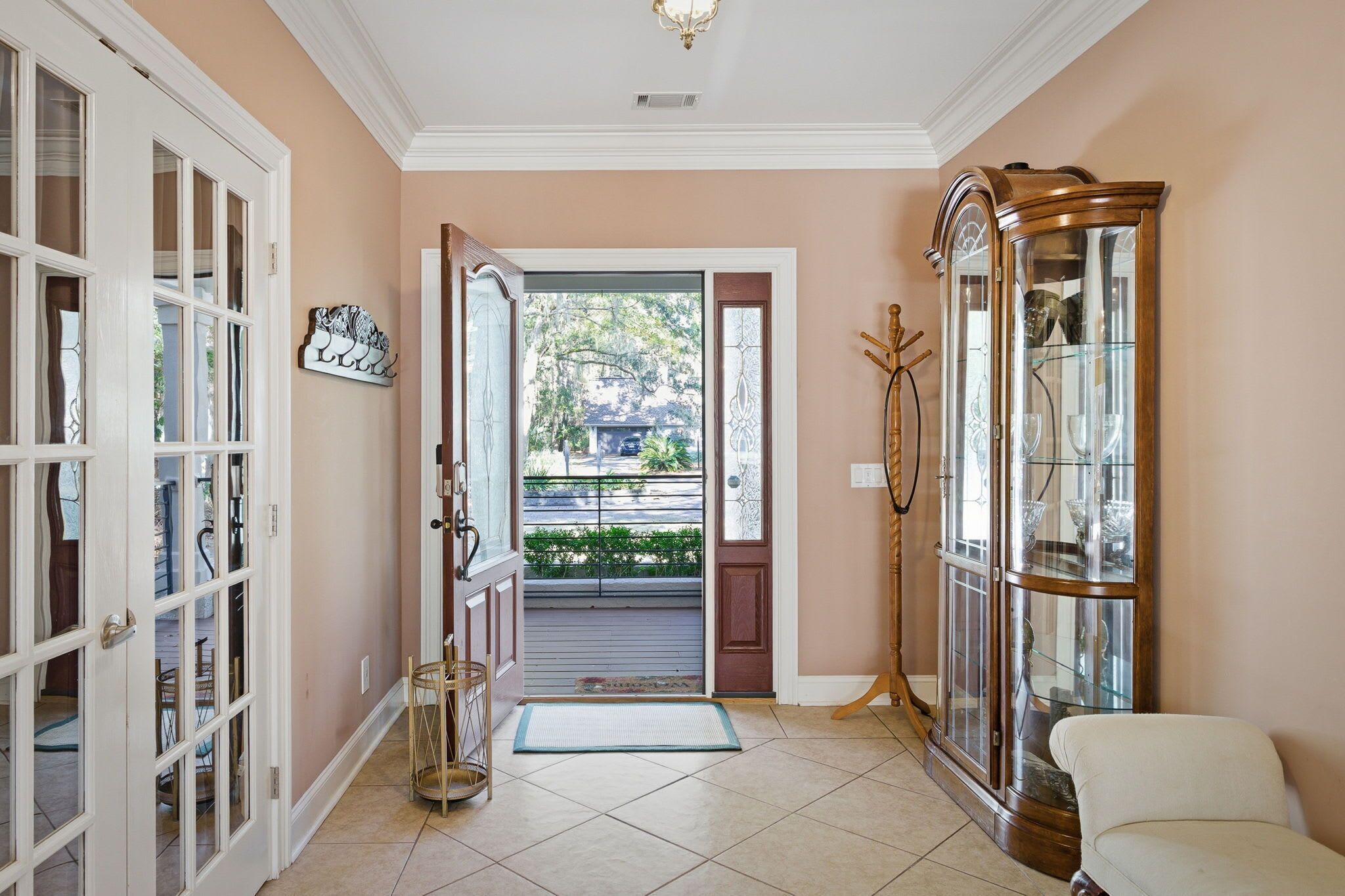A hallway with a glass cabinet, a door leading outside, and a mat at the entrance.