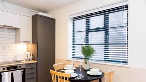 Una cucina moderna con zona pranzo, con un tavolo nero apparecchiato per quattro persone, una macchina per il caffè e un'ampia finestra con persiane.