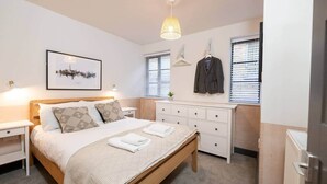 Una camera da letto con un letto, comodini, una cassettiera, un appendiabiti e un quadro appeso al muro.