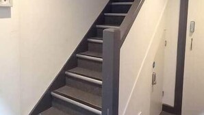 Een trap met een leuning, beklede treden en een deur onderaan.
